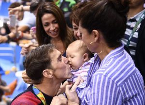 USA’s Michael Phelps (L) kisses his son Boomer next to his partner Nicole Johnson after he won the Men’s 200m Butterfly Final during the swimming event at the Rio 2016 Olympic Games at the Olympic Aquatics Stadium in Rio de Janeiro on August 9, 2016.