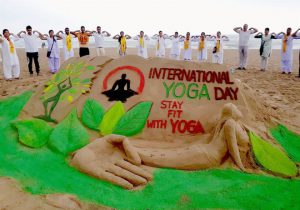 Some people practice yoga near a sand sculpture by artist Manas Sahoo on the eve of International Day of Yoga at a beach in Puri, Odisha, on June 20, 2017