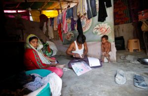 A man from the Rohingya community fills out an identification form, provided by local police, as his wife and daughter sit next to him inside their shack at a camp in New Delhi, October 4, 2018